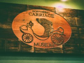 A beautiful rustic redwood sign made out of multiple adjoining planks, with the Northwest Carriage Museum logo standing up from a cleanly debossed oval in the center, creating a contrast to the surrounding aged planks