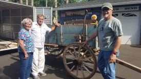 Curator Jerry Bowman with the donators of the Mitchell Wagon standing in front of the rustic farm wagon in its pre-conservation condition.