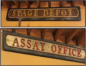 Two wooden signs with brightly painted letters in relief reading "Stage Depot" and "Assay Office"