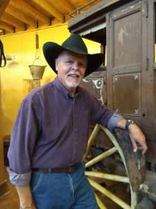NWCM curator, Jerry Bowman, standing in front of an 1888 Stagecoach, wearing an impressive cowboy hat.